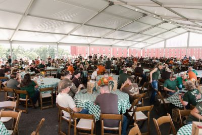Large group of men and women at tables under a tent